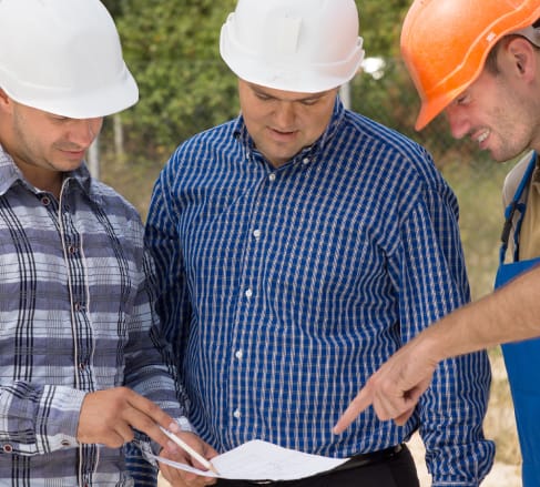 image of three male employees wearing construction hard hats looking at a diagram overjoyed with their new Franklin, TN Contactor's Insurance.